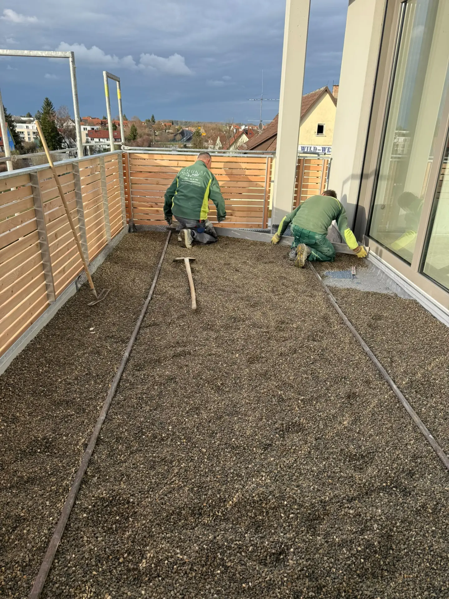 Zwei Mitarbeiter ziehen das Splittbett auf dem Balkon mit Lehren ab