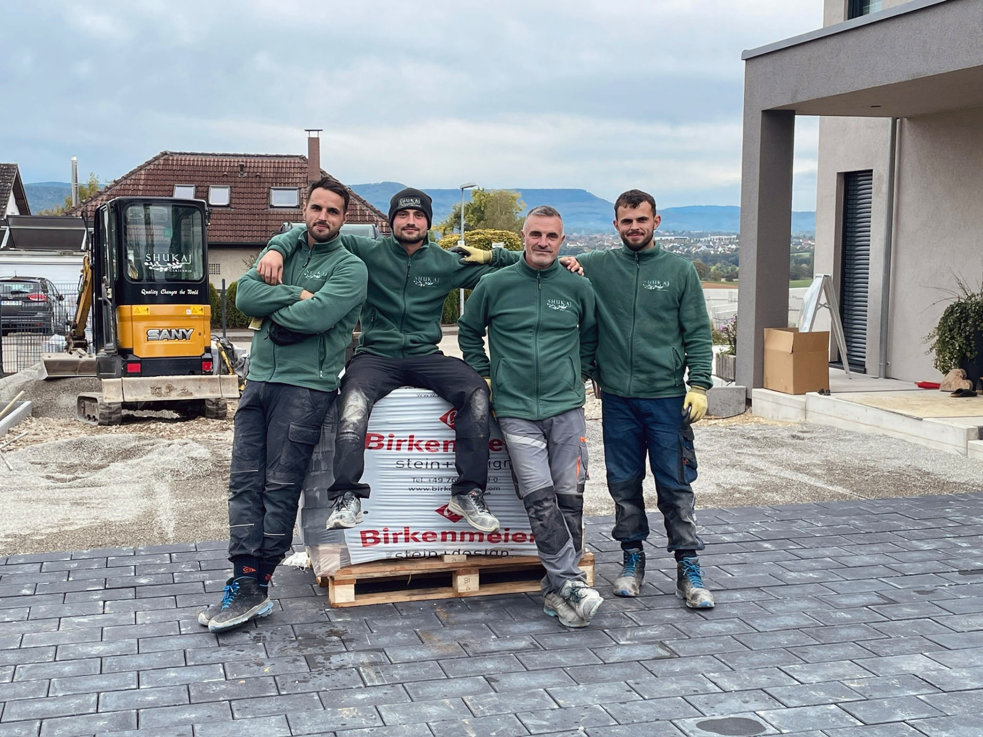 Team von Shukaj Gartenbau in grüner Arbeitskleidung auf einer frisch gepflasterten Hoffläche