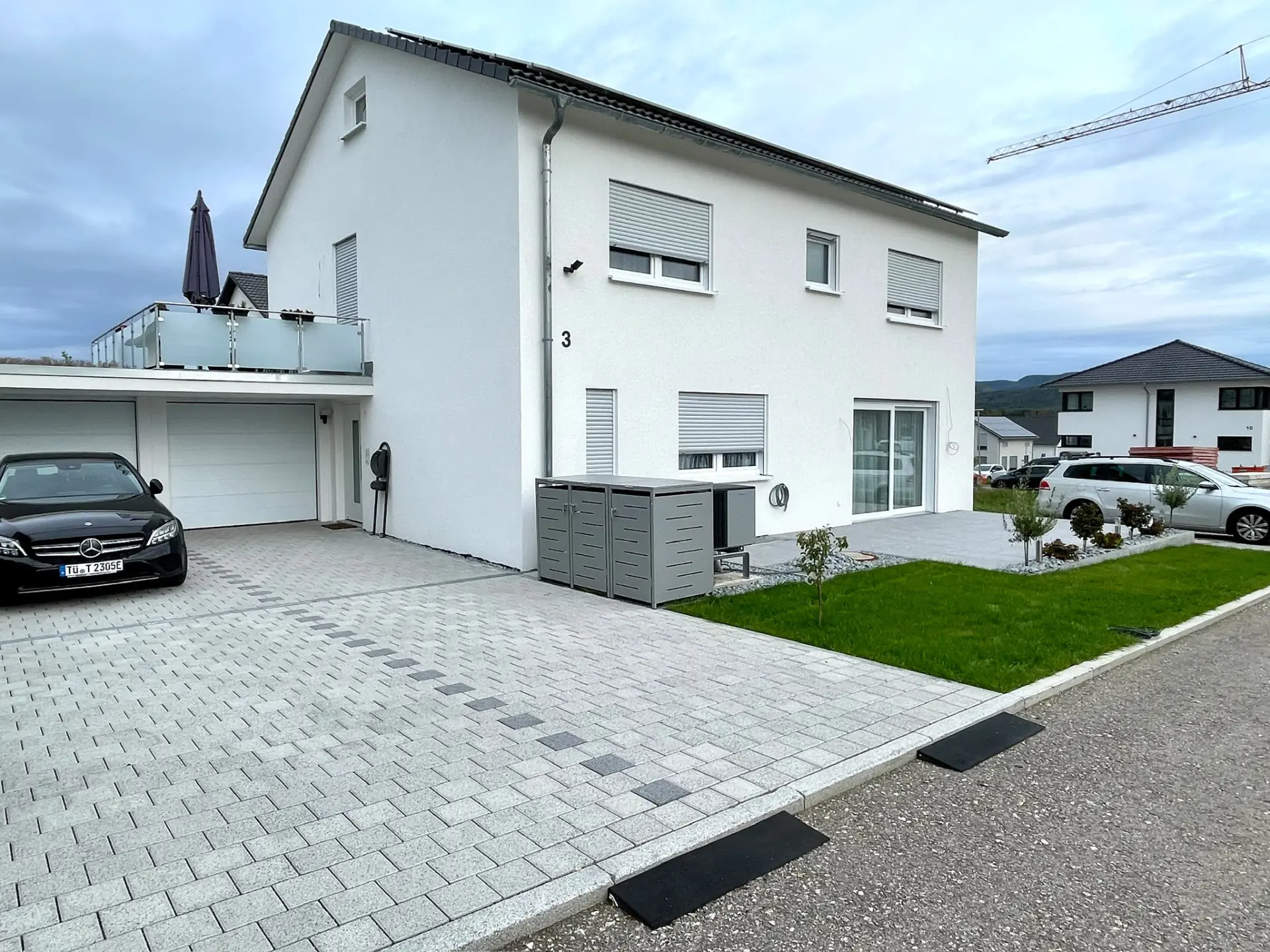 Fertige Außenanlage mit gepflasterter Zufahrt, Rasenfläche und neu gepflanzten Bäumen