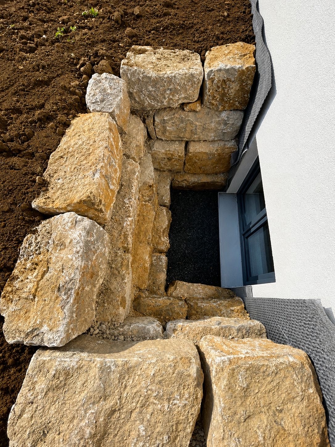 Neu gesetzte Natursteinmauer aus großen Sandsteinblöcken zur Hangsicherung an einem Hausfundament