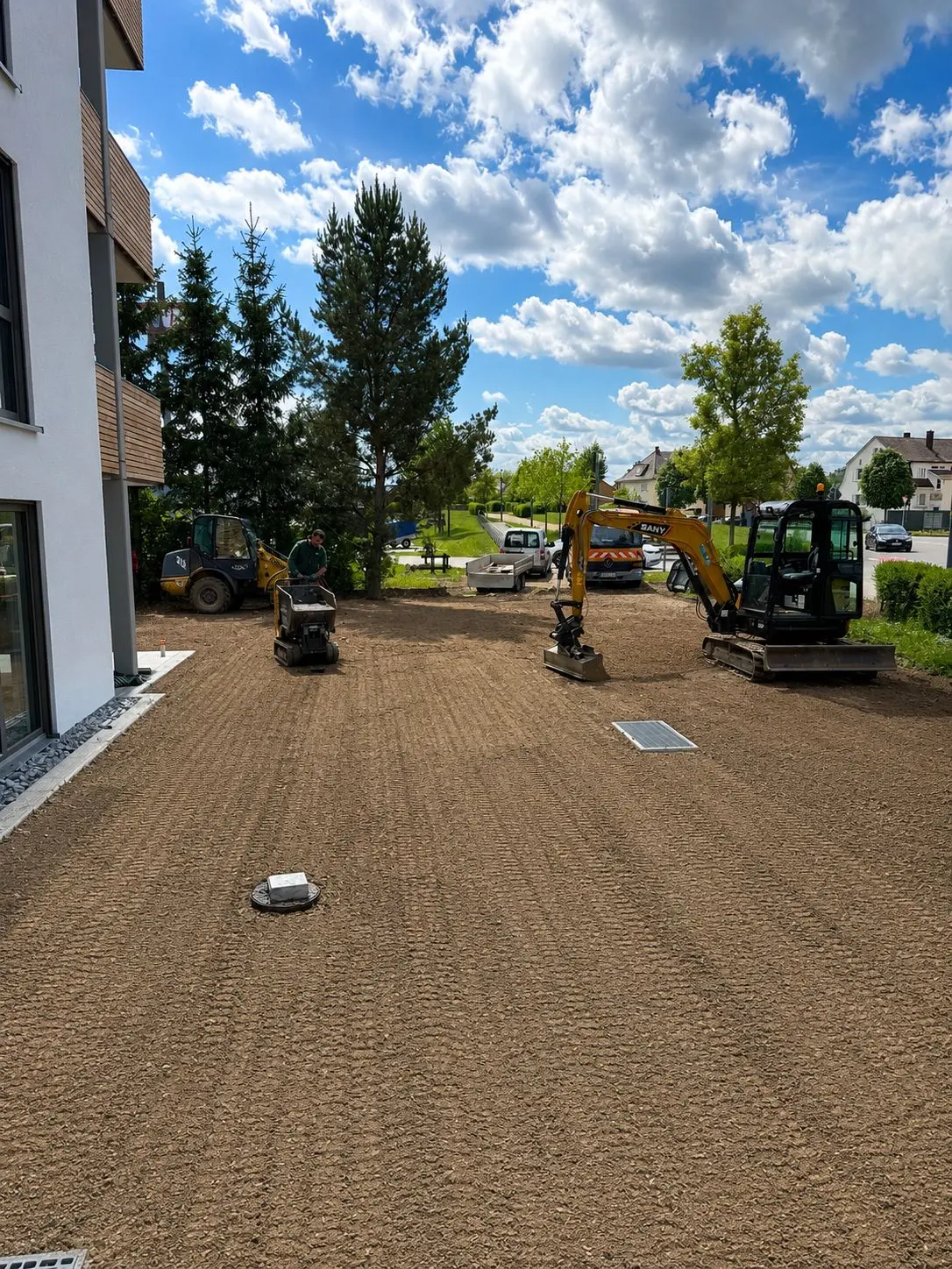 Frisch reguliertes und verdichtetes Planum mit Rüttelplatte und Minibagger vor einem Neubau